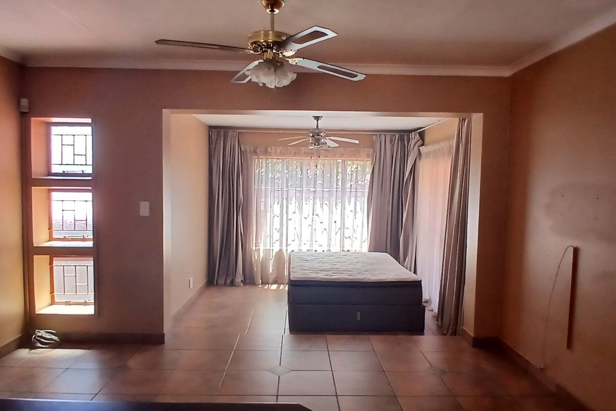Spacious living area featuring tiled flooring, ceiling fans, and natural light through casement windows, offering a versatile layout for comfortable family living.