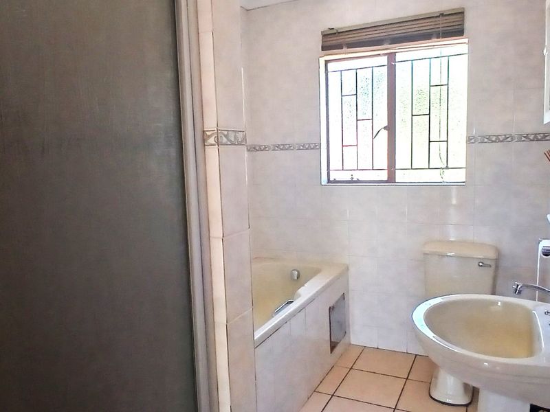 A functional bathroom featuring a built-in bathtub, pedestal sink, toilet, and shower enclosure with tiled finishes and security bars on the window.