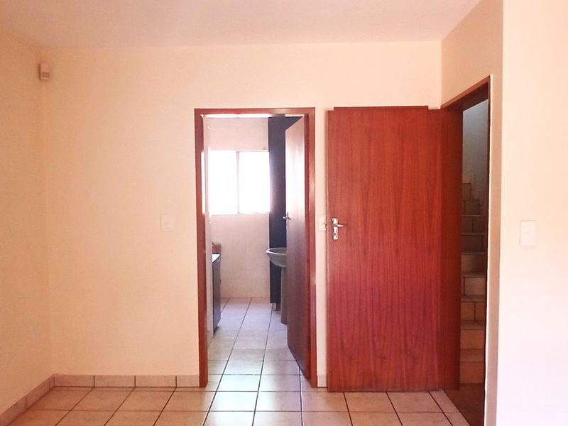 An empty bedroom featuring tiled flooring and a built-in wardrobe, with direct access to an adjacent bathroom and staircase.
