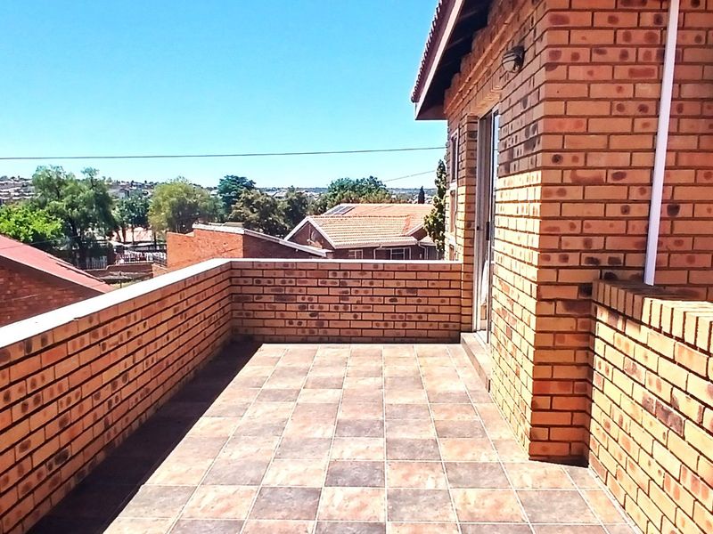 An elevated balcony featuring face brick walls, tiled flooring, and an external solar water heater unit, offering an open outdoor space.