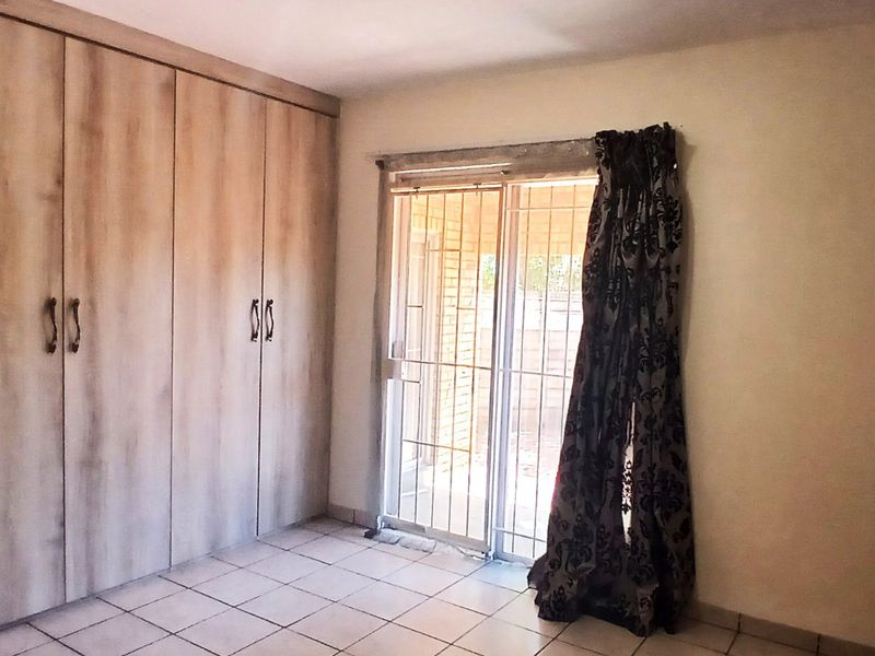 A bedroom featuring tiled flooring, extensive built-in cupboards, and a sliding glass door with a security gate providing access to the exterior.