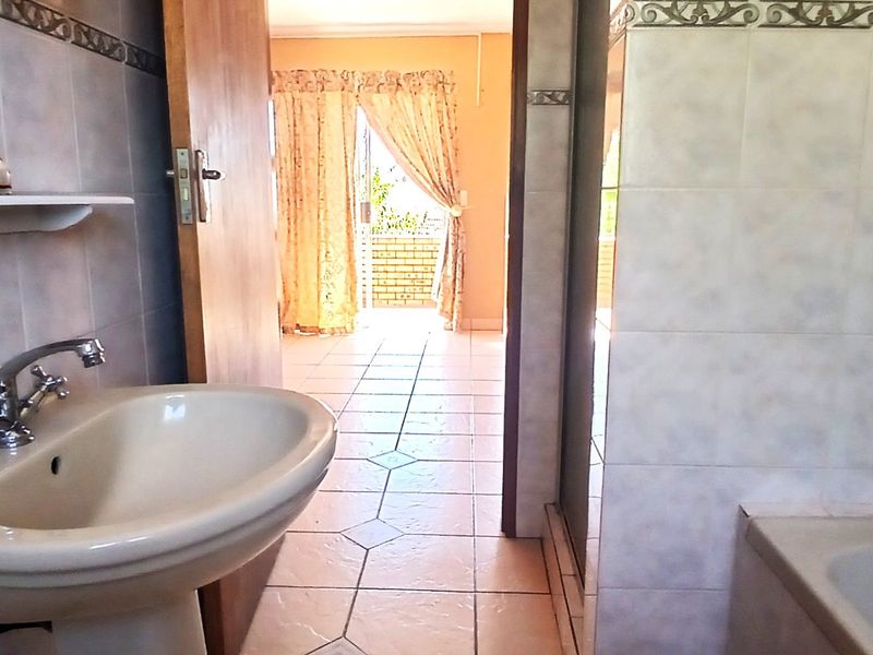 A dated bathroom featuring a pedestal basin, tiled walls, and a built-in bathtub, with a view through to an adjacent room.