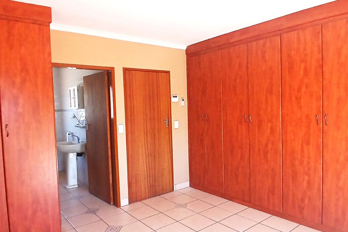 Spacious bedroom featuring extensive built-in wooden cabinetry, tiled flooring, and direct access to an en-suite bathroom.