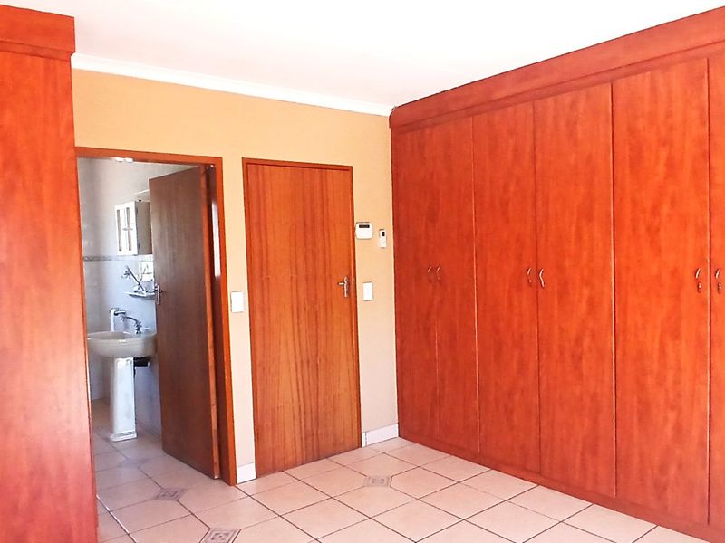 Spacious bedroom featuring extensive built-in wooden cabinetry, tiled flooring, and direct access to an en-suite bathroom.