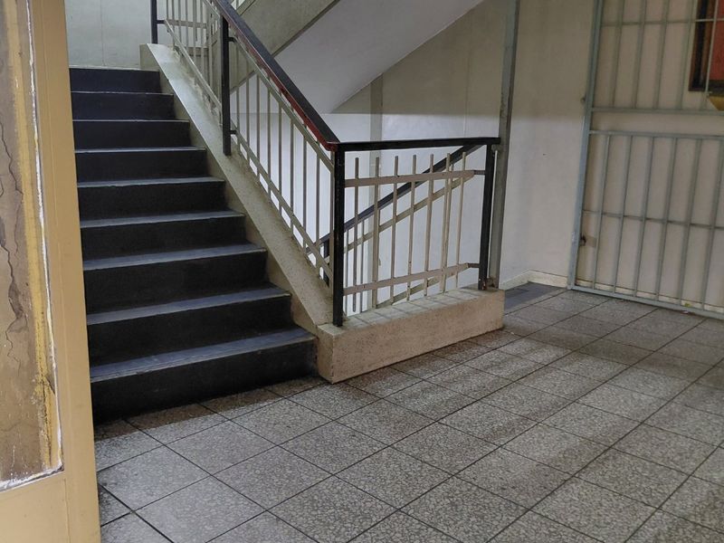 A communal apartment building stairwell featuring tiled flooring, metal safety railings, and a security gate leading to an emergency exit.