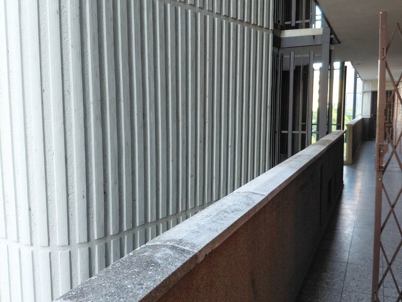 An exterior balcony area featuring tiled flooring, a concrete balustrade, and textured architectural facade elements.