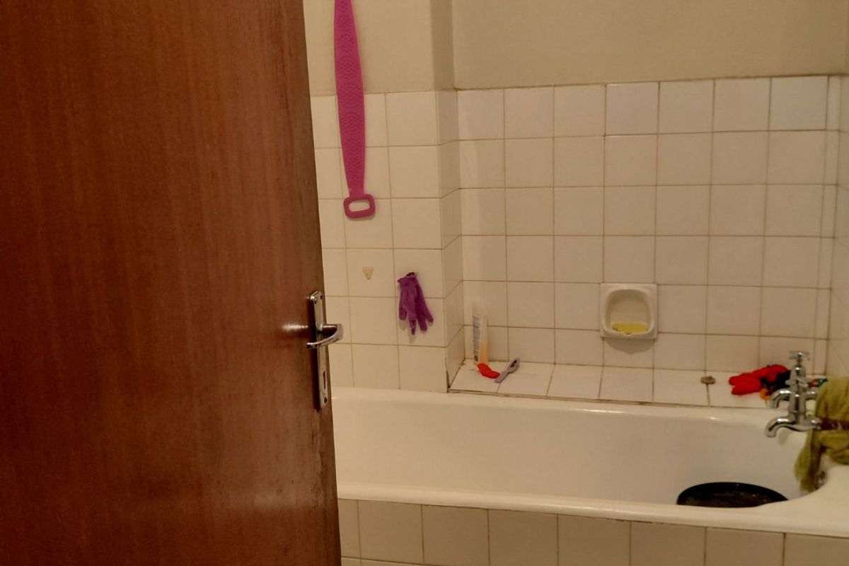 A functional bathroom featuring a standard bathtub with tiled surround and a high-level window with security bars.