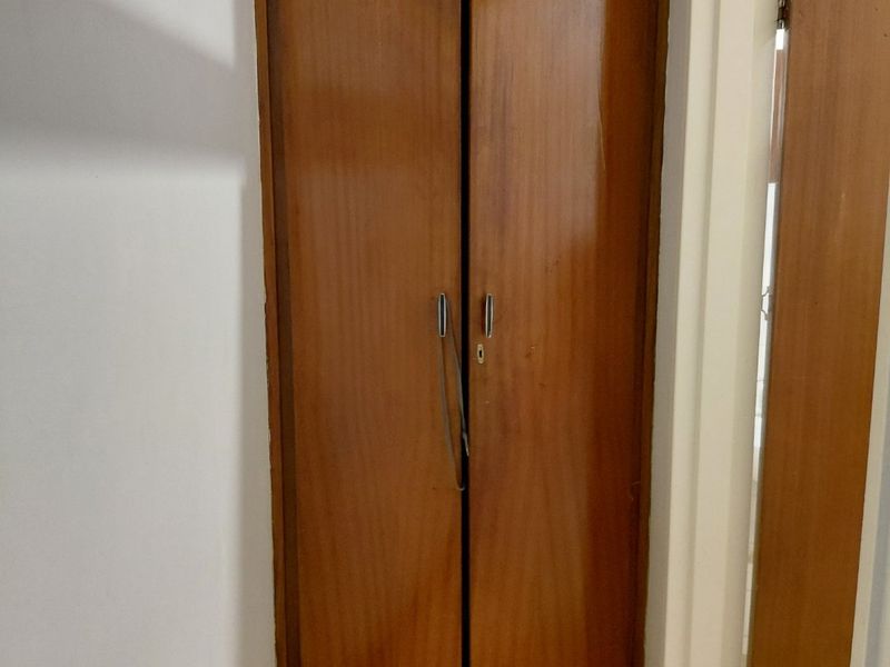 A hallway featuring a built-in wooden cupboard with overhead storage and tiled flooring, showing signs of age and wear.