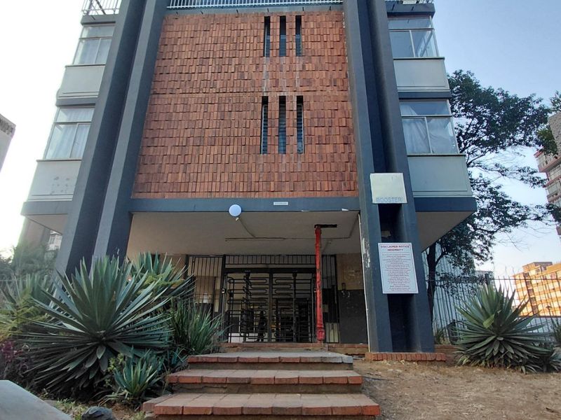 Front elevation of a multi-story apartment building featuring brick facade detailing, concrete entrance stairs, and secure gated access.