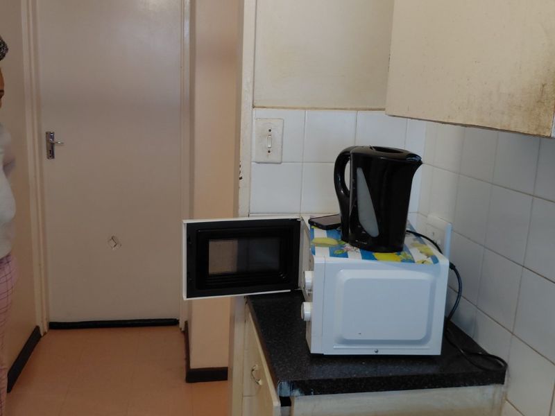 A compact kitchen area featuring built-in cabinetry, a tiled backsplash, and an electric stove, showing signs of wear and requiring cosmetic updates.