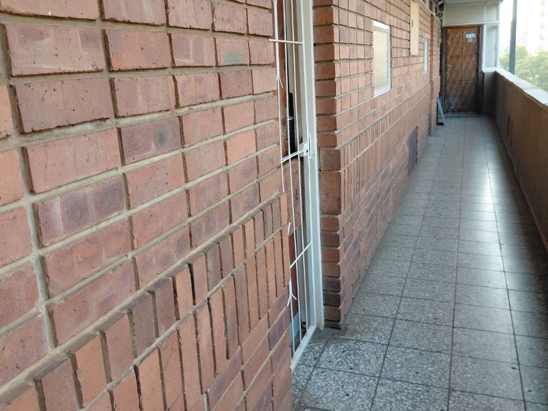 An exterior apartment hallway featuring exposed brick walls and tiled flooring with a security gate entrance.