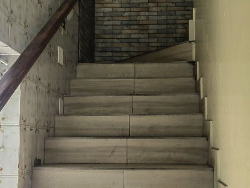 A staircase featuring tiled steps, a wooden handrail, and a decorative brick-style feature wall.