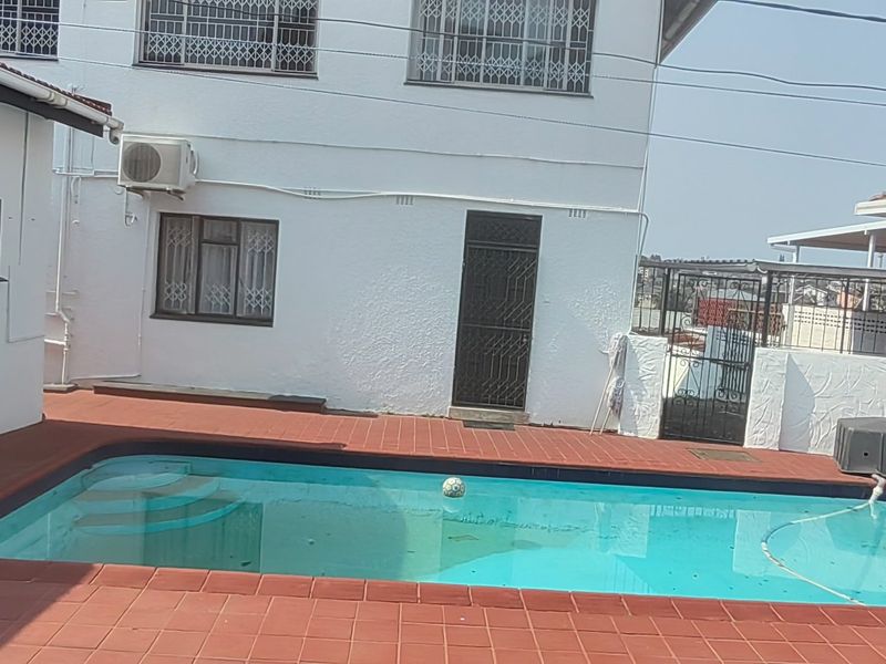 Outdoor pool area featuring a tiled deck, security features on windows and doors, and an exterior air conditioning unit.