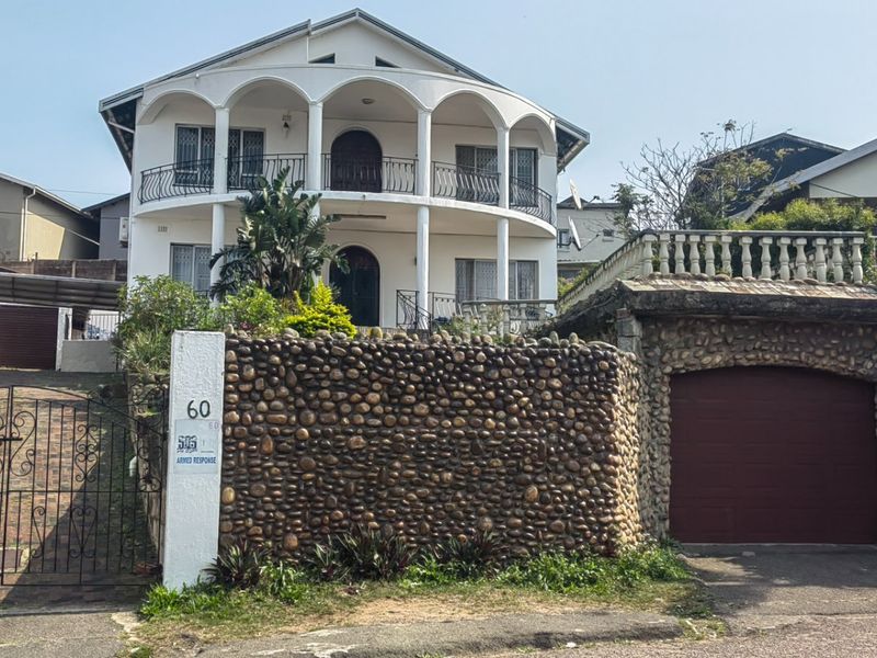 Front elevation of a multi-story townhouse featuring a stone-clad boundary wall, arched balcony with wrought iron railings, and a private garage.