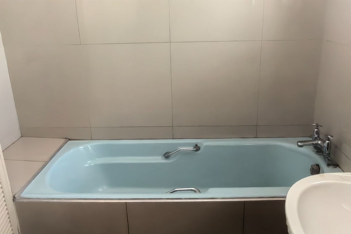 A functional bathroom featuring a built-in bathtub, basin, and neutral wall tiling, offering a blank canvas for modern updates.