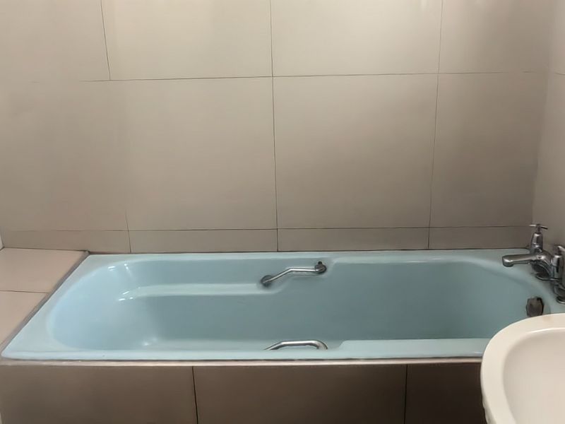 A functional bathroom featuring a built-in bathtub, basin, and neutral wall tiling, offering a blank canvas for modern updates.