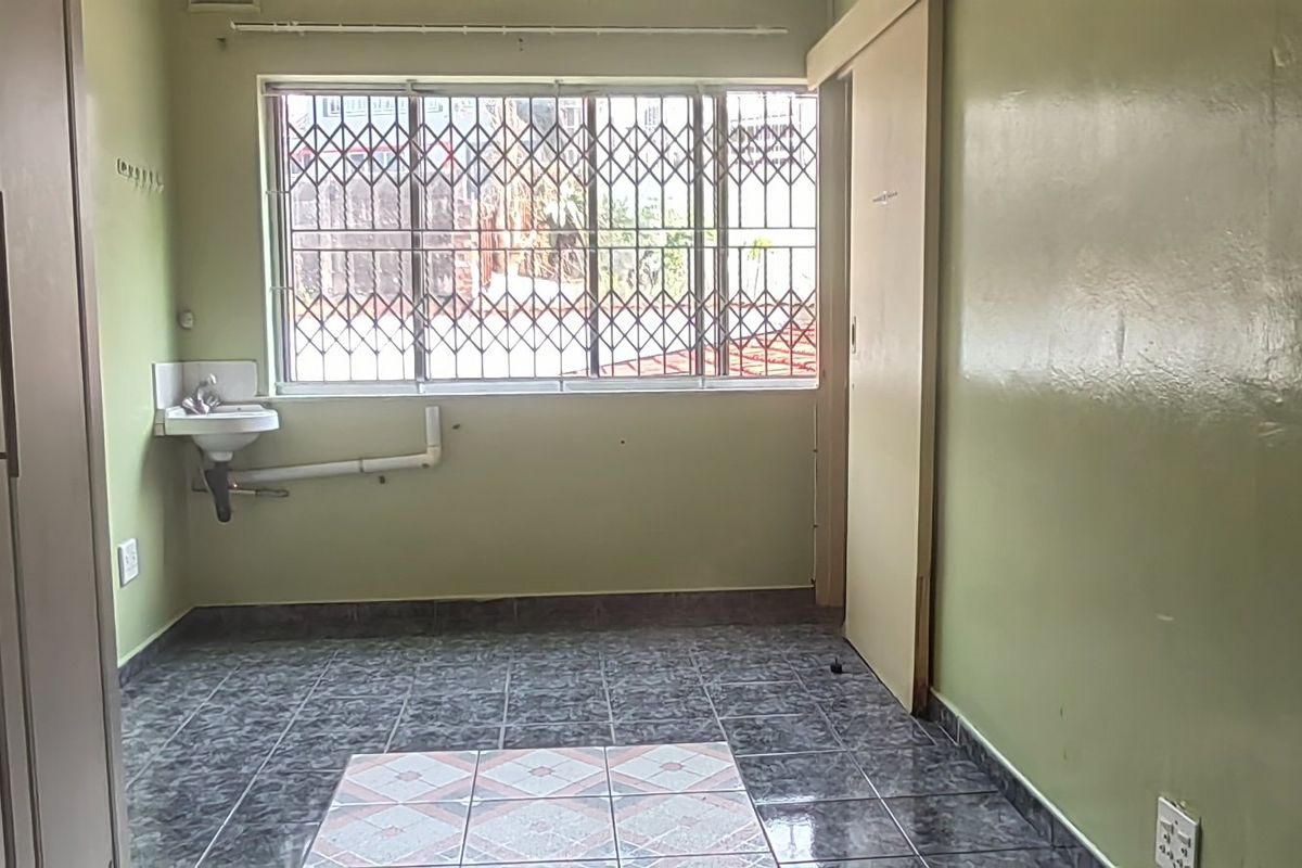 An empty bedroom featuring tiled flooring, built-in cupboards, and a wall-mounted basin with exposed plumbing.
