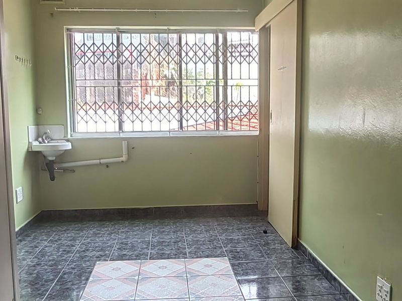 An empty bedroom featuring tiled flooring, built-in cupboards, and a wall-mounted basin with exposed plumbing.
