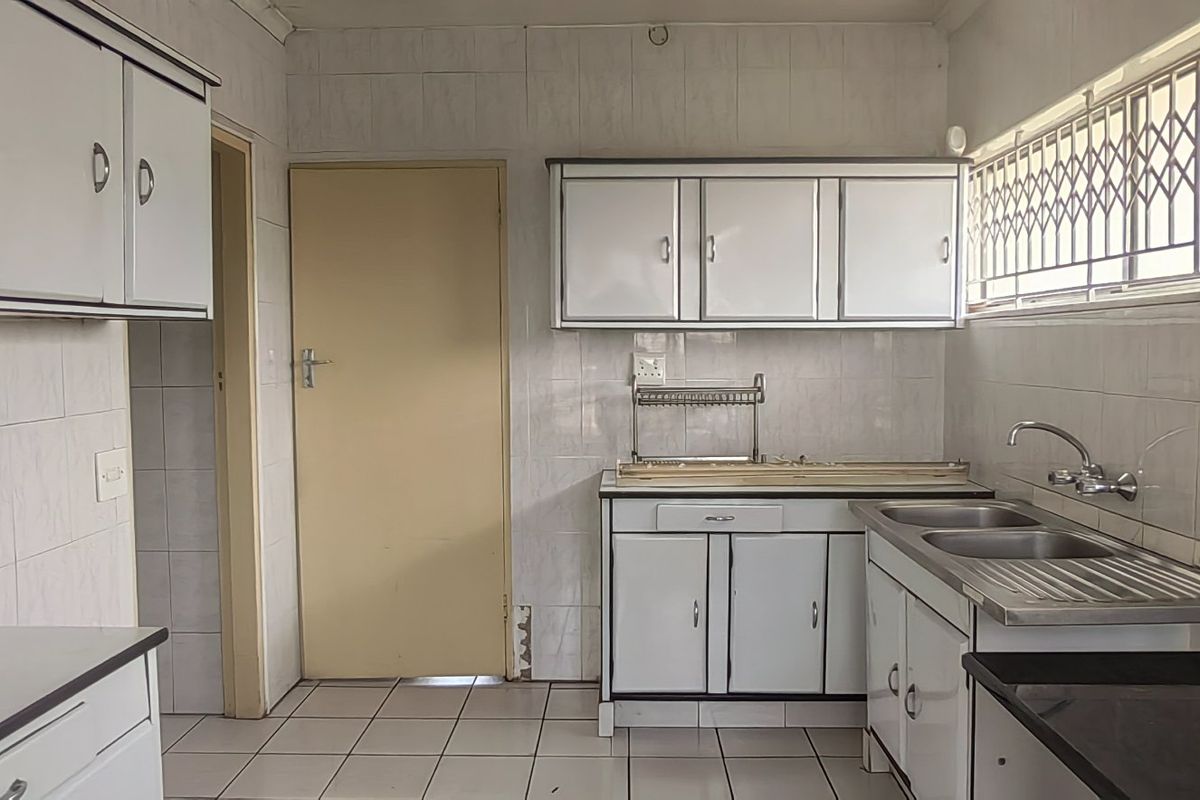A functional kitchen featuring tiled walls, built-in cabinetry, and a double stainless steel sink, offering a blank canvas for potential modernization.