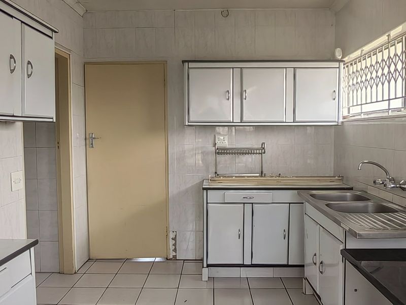 A functional kitchen featuring tiled walls, built-in cabinetry, and a double stainless steel sink, offering a blank canvas for potential modernization.