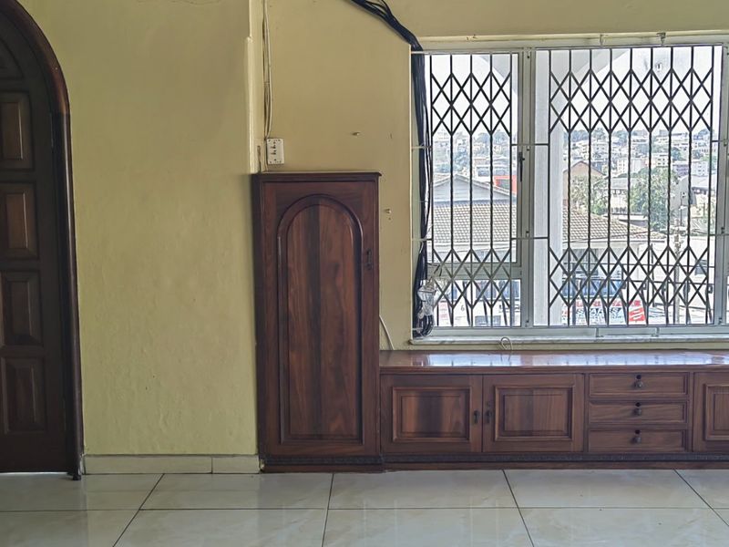 Living area featuring built-in wooden cabinetry, tiled flooring, and an arched door, with a window fitted with a security gate.