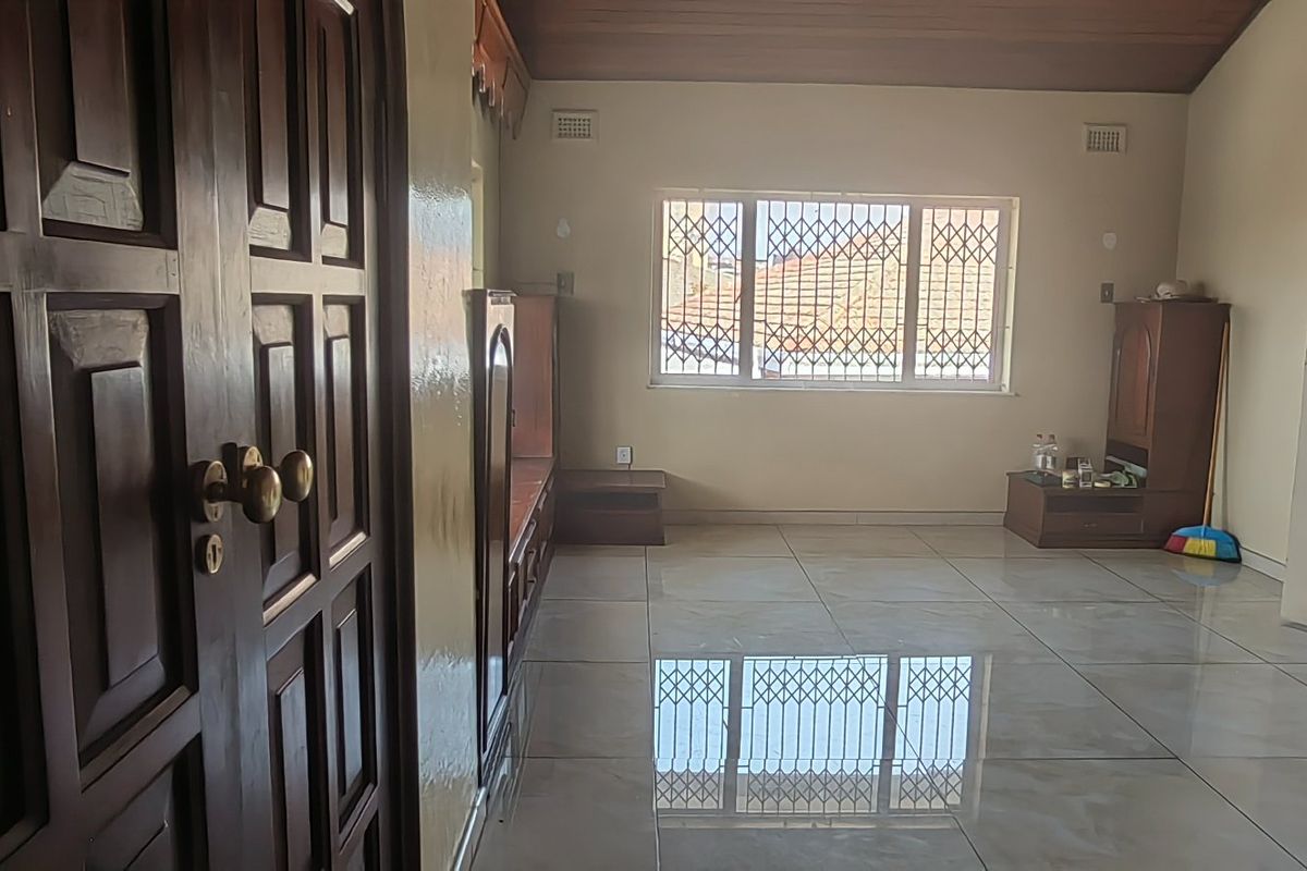 Spacious living area featuring polished tiled flooring, timber ceiling, and a window fitted with security bars.