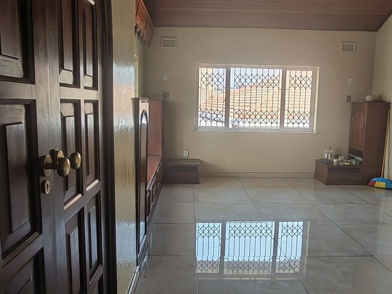 Spacious living area featuring polished tiled flooring, timber ceiling, and a window fitted with security bars.