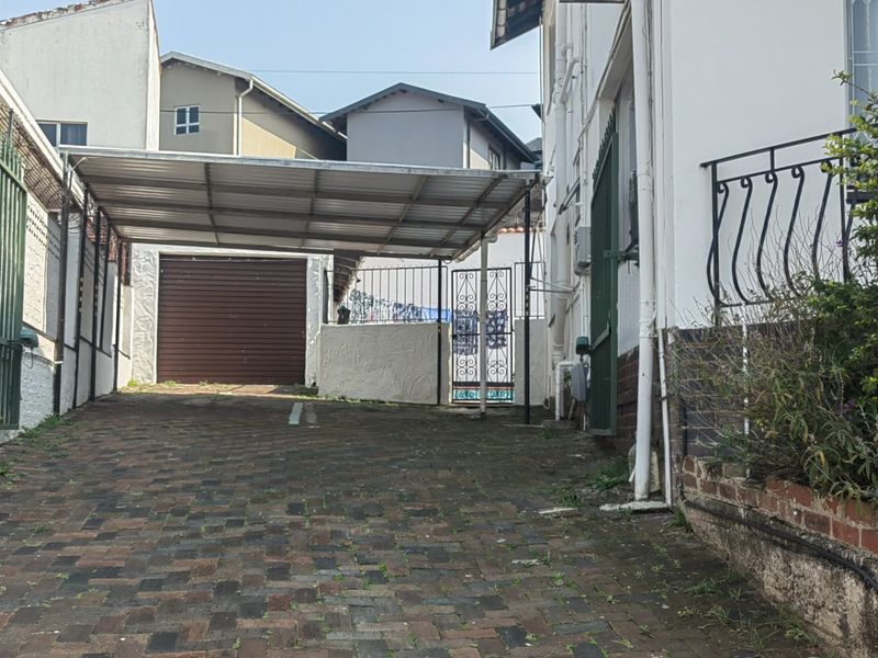 Front exterior view of the townhouse featuring a paved driveway, covered carport, and secure gated entrance with boundary walls.