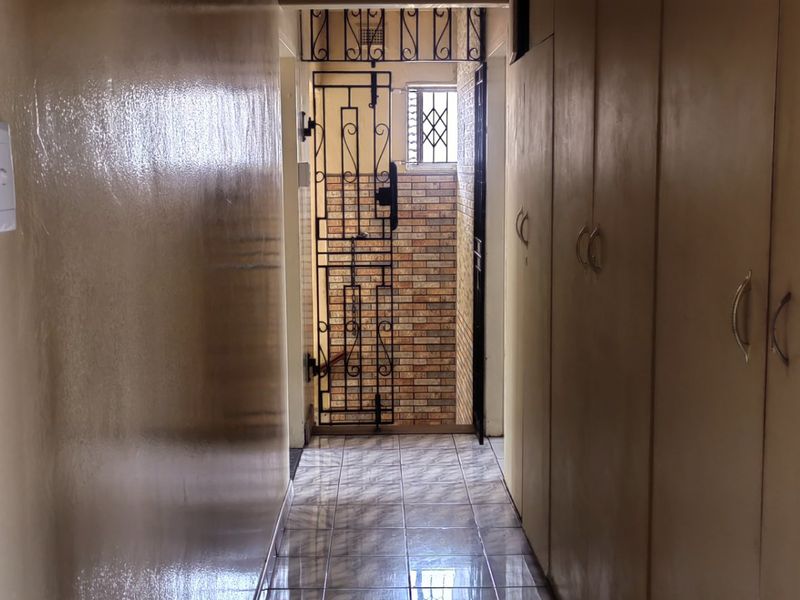 A functional hallway featuring built-in storage cupboards, tiled flooring, and a secure metal gate leading to the exterior.