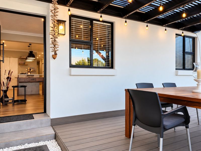 A well-maintained covered patio featuring composite decking, a modern pergola with string lighting, and direct access to the interior living space.