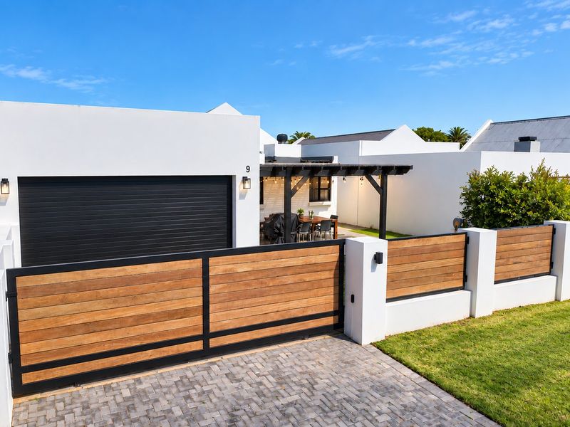 Modern front facade featuring a sleek black garage door, timber-accented boundary fencing, a paved driveway, and a covered pergola area.