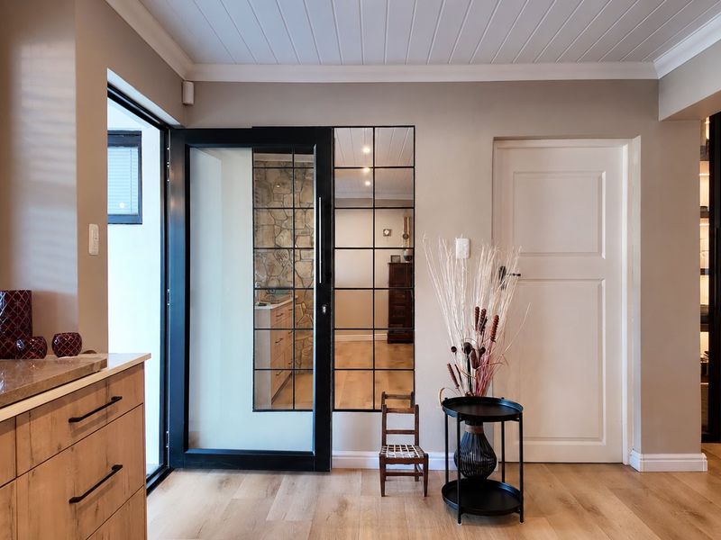 Modern entrance area featuring laminate flooring, sleek built-in cabinetry with stone countertops, and stylish black-framed glass doors leading to adjacent living spaces.
