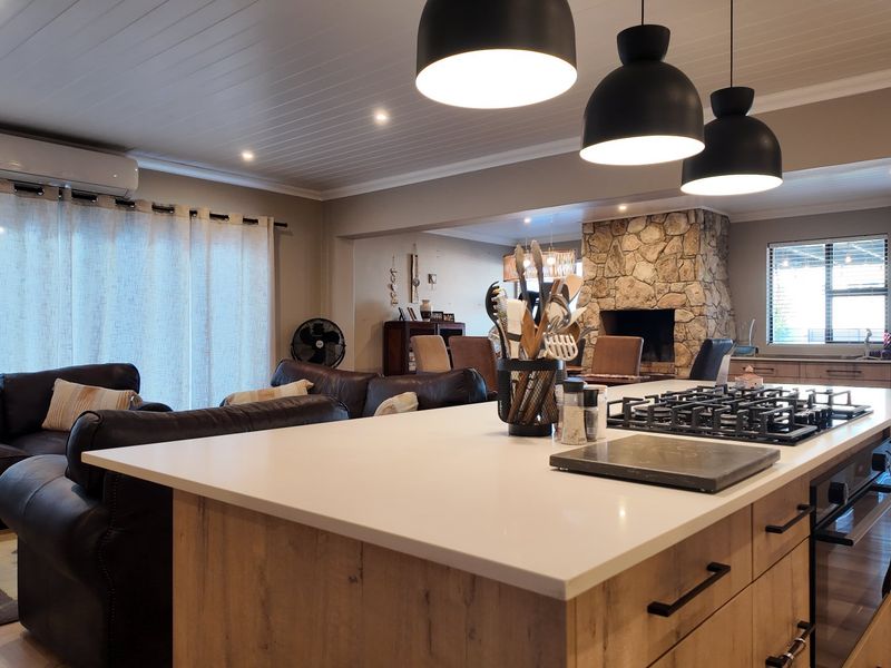 Spacious open-plan living area featuring a modern kitchen island with gas cooktop, stone fireplace, and stylish pendant lighting, creating a warm, functional family space.