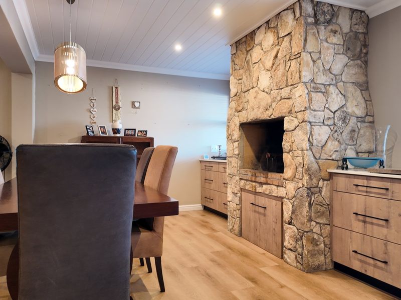 Dining area featuring a prominent stone fireplace, modern built-in cabinetry, light wood-look laminate flooring, and a clean tongue and groove ceiling finish.