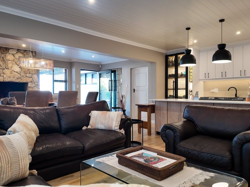 Spacious open-plan living area featuring a stone fireplace, modern kitchen with island, pendant lighting, and timber flooring throughout.