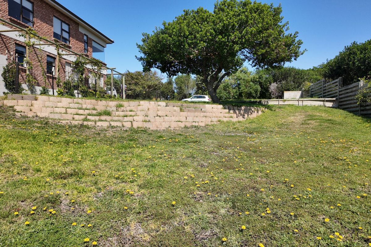 A spacious rear garden area featuring a tiered retaining wall, mature tree, and perimeter timber fencing, offering potential for landscaping and outdoor development.