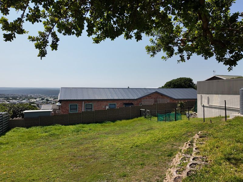 A rear view of the residential property featuring a grassy yard, perimeter fencing, and a water tank with a distant landscape view.