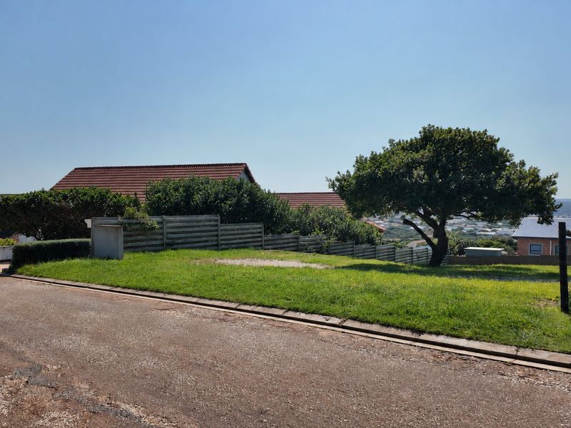 A vacant residential plot featuring a well-maintained grass lawn, mature tree, and timber fencing, situated along a paved street.
