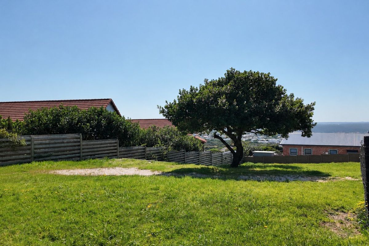 A well-maintained residential plot featuring a grassy lawn, a mature tree, and timber boundary fencing with surrounding neighborhood views.