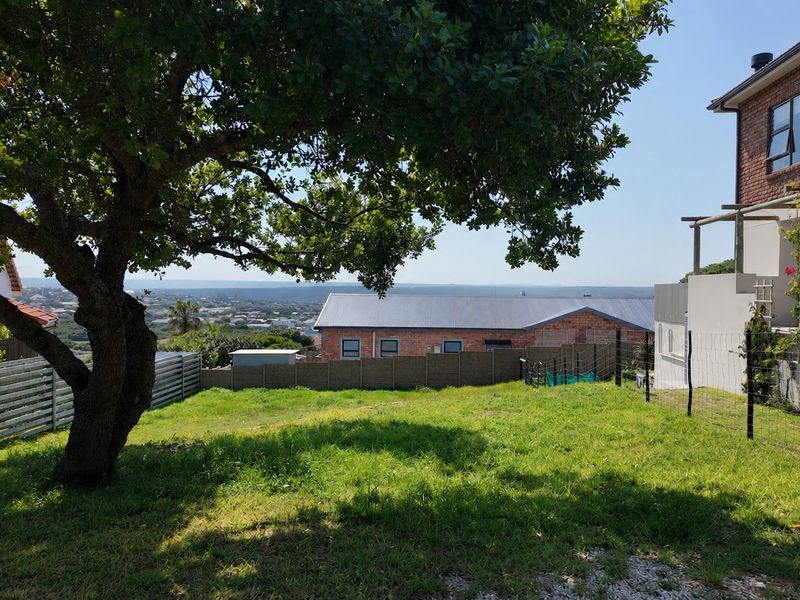 A view of the residential garden area featuring established trees, perimeter fencing, and a view of the surrounding neighborhood.