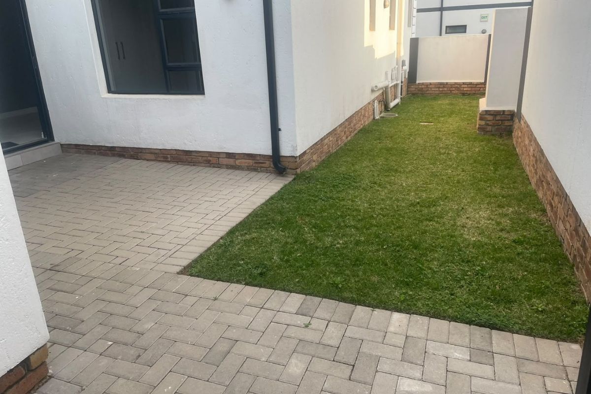 A neat rear courtyard featuring a paved patio area and a small private lawn, enclosed by brick boundary walls.