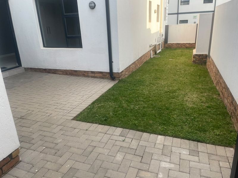 A neat rear courtyard featuring a paved patio area and a small private lawn, enclosed by brick boundary walls.