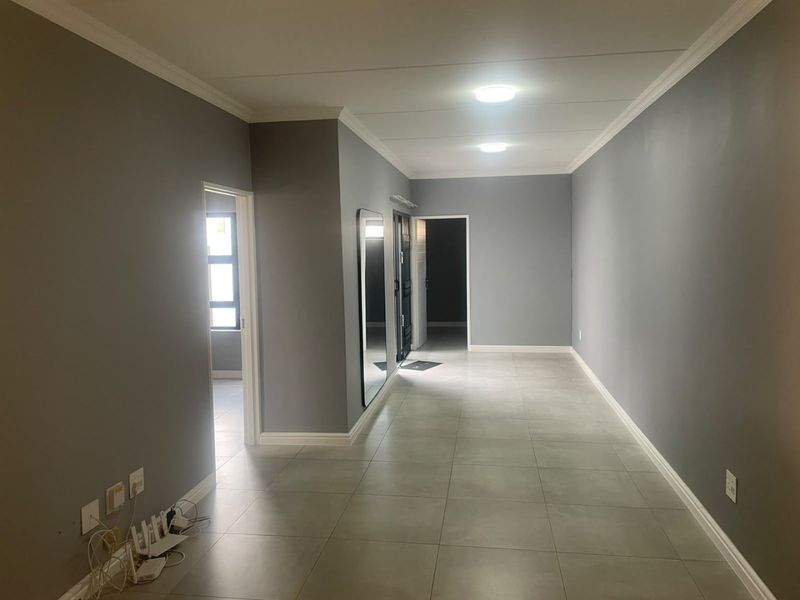 A spacious, neutrally painted hallway featuring large format floor tiles, clean lines, and recessed ceiling lighting, providing a bright and modern transition space.