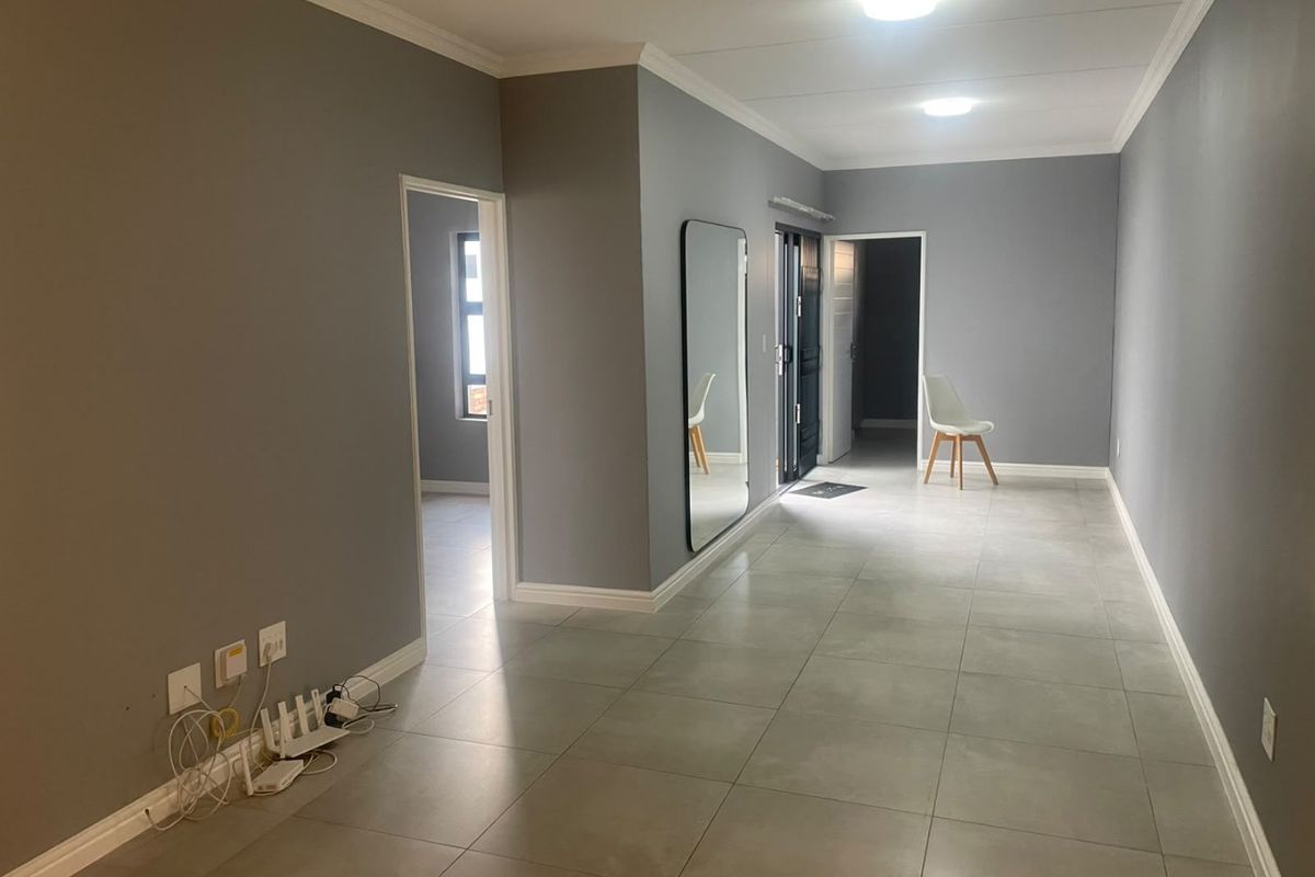 A spacious, neutrally painted living area featuring large format floor tiles, modern ceiling lighting, and clean architectural lines throughout the open-plan space.