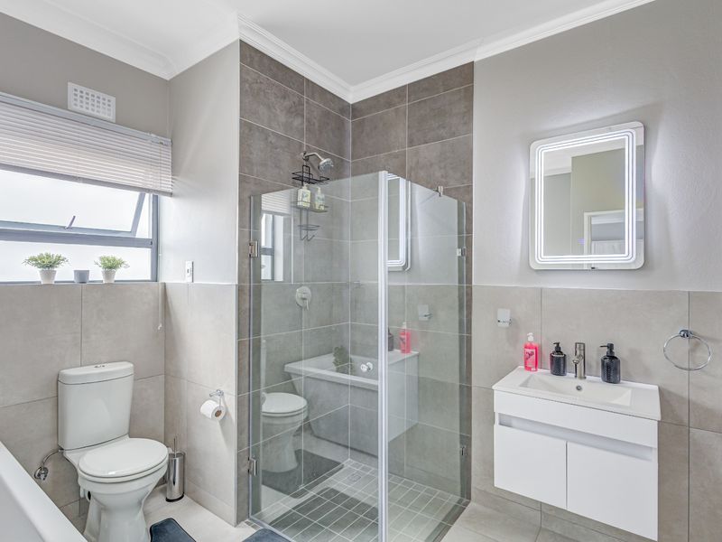 Modern bathroom featuring a glass-enclosed shower, separate bathtub, wall-mounted vanity with basin, and an illuminated mirror, finished with contemporary neutral tiling.