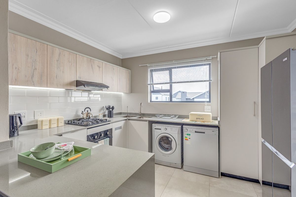 Modern kitchen featuring light wood-tone cabinetry, quartz countertops, subway tile backsplash, and integrated space for laundry and dishwasher appliances.