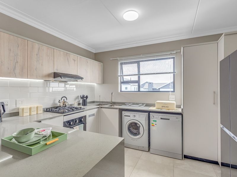 Modern kitchen featuring light wood-tone cabinetry, quartz countertops, subway tile backsplash, and integrated space for laundry and dishwasher appliances.