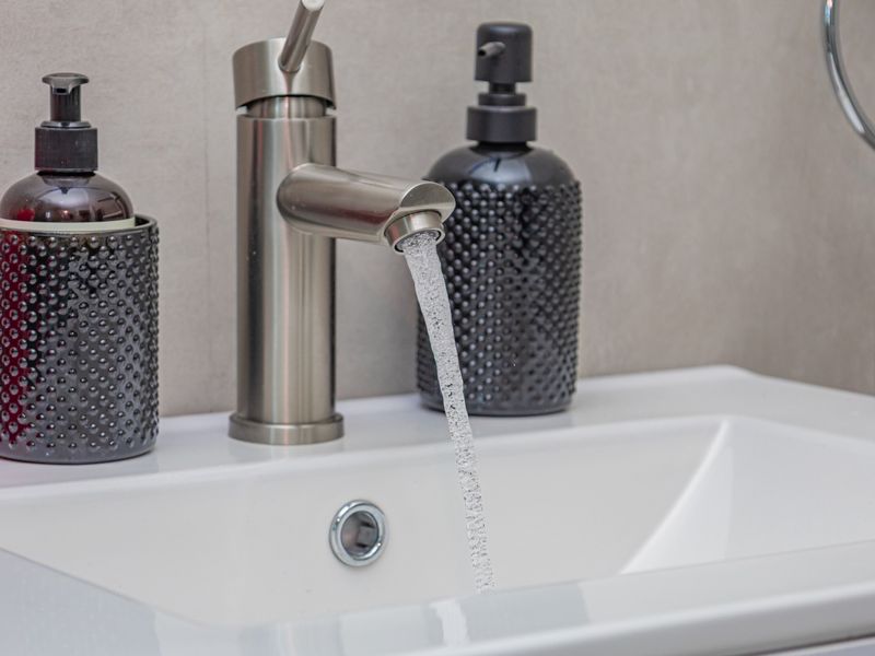 Close-up view of a modern bathroom basin featuring a sleek stainless steel mixer tap and neutral wall tiling.