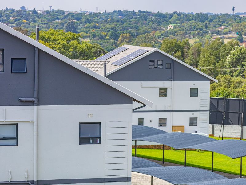Exterior view of townhouse complex featuring modern grey and white facades, solar panels, and covered carport parking areas.