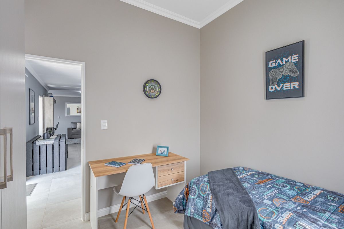 A well-maintained bedroom featuring neutral wall tones, crown molding, and tiled flooring, with a clear view into the adjacent living area.